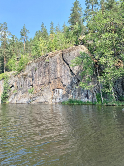 Jyrkkä kallio kuvattuna järveltä aurinkoisena päivänä.